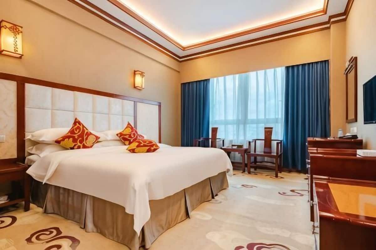 A hotel room with a large bed, a desk, a chair, and a window with curtains.