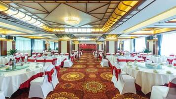 A banquet hall with rows of tables, white tablecloths, and red sashes.