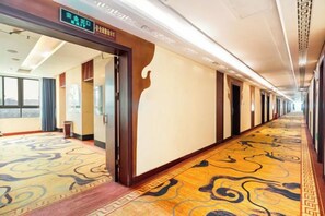 A hotel corridor with a patterned carpet, doors on the right, and a window on the left. - Pingguo International Hotel (Pingguo)