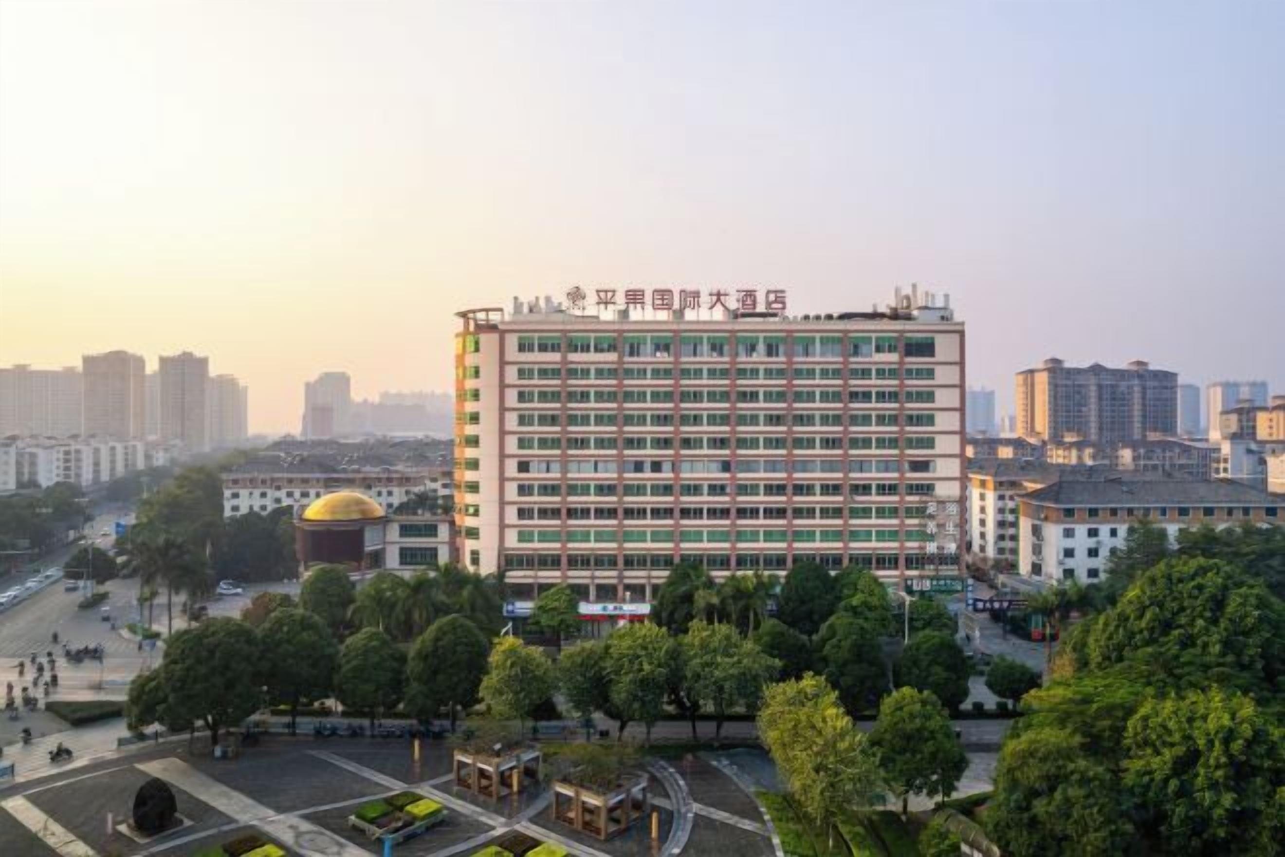 A multi-story hotel with a central courtyard, surrounded by trees and other buildings.