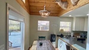 Ein Essbereich mit Holztisch und Stühlen, eine Küche mit Bar und eine Decke mit aufgehängten Hirschköpfen.