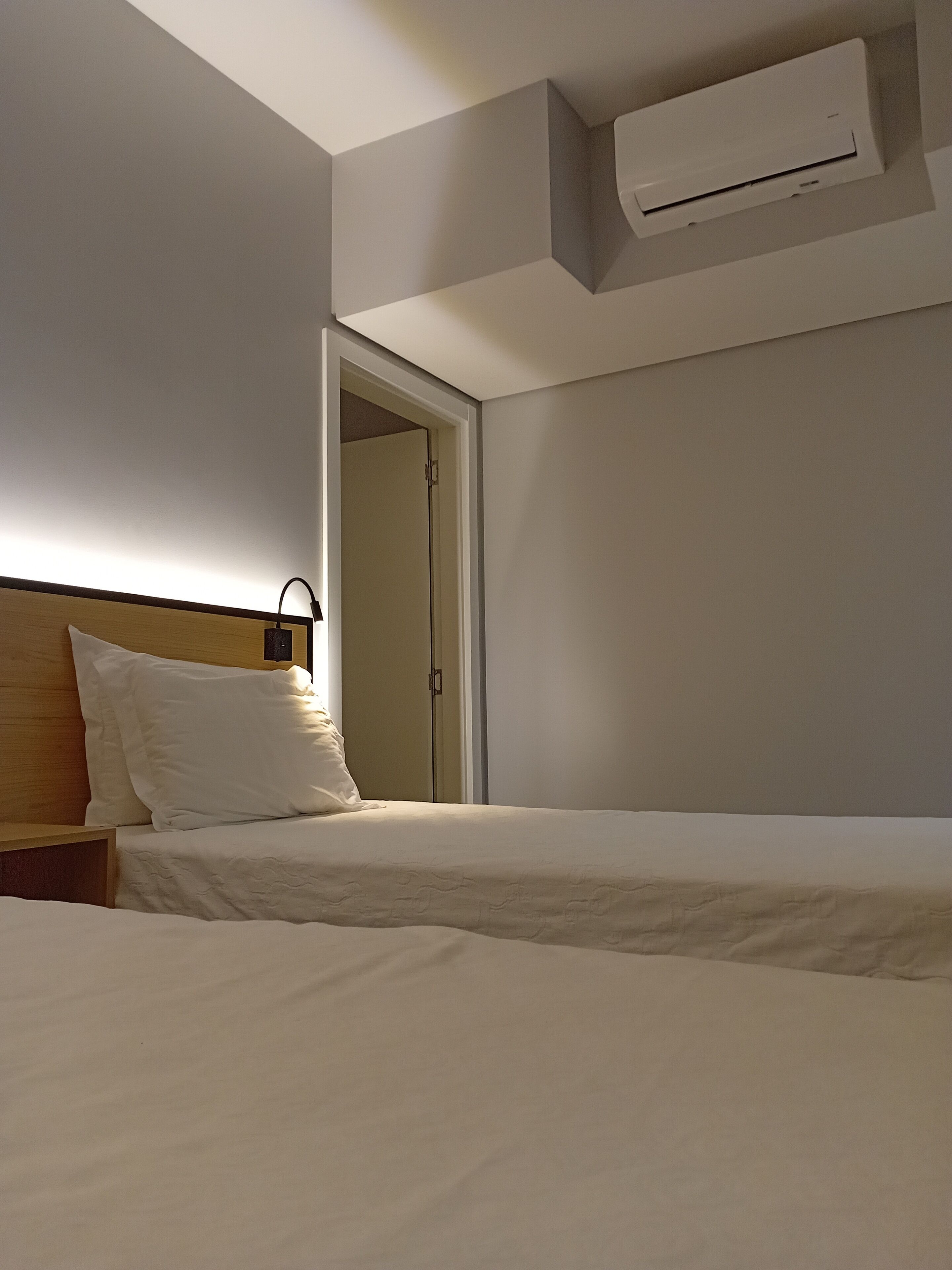 A hotel room with a bed, a nightstand, a lamp, and an air conditioning unit mounted on the wall.