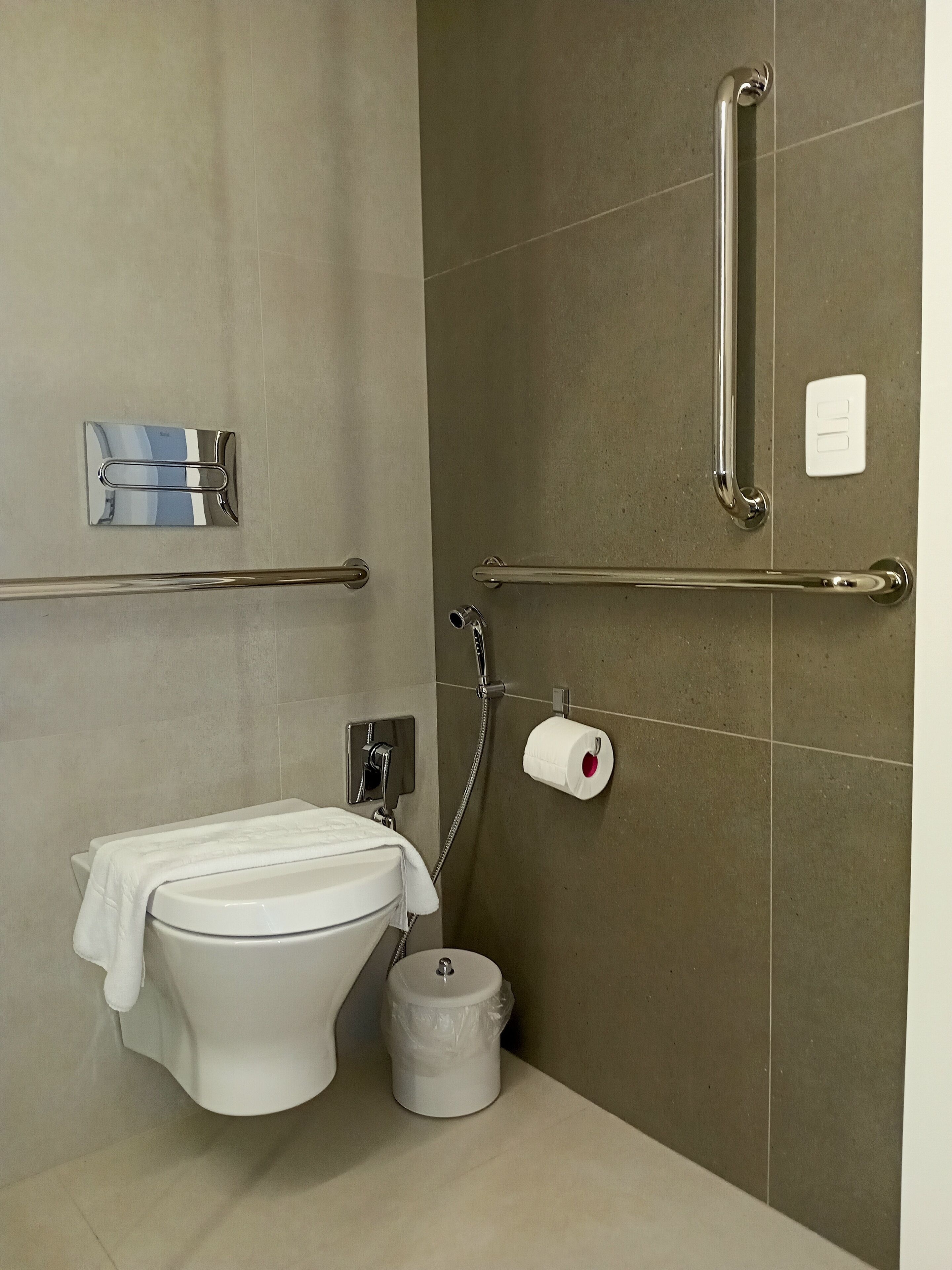 A modern bathroom with a toilet, bidet, and handrails.