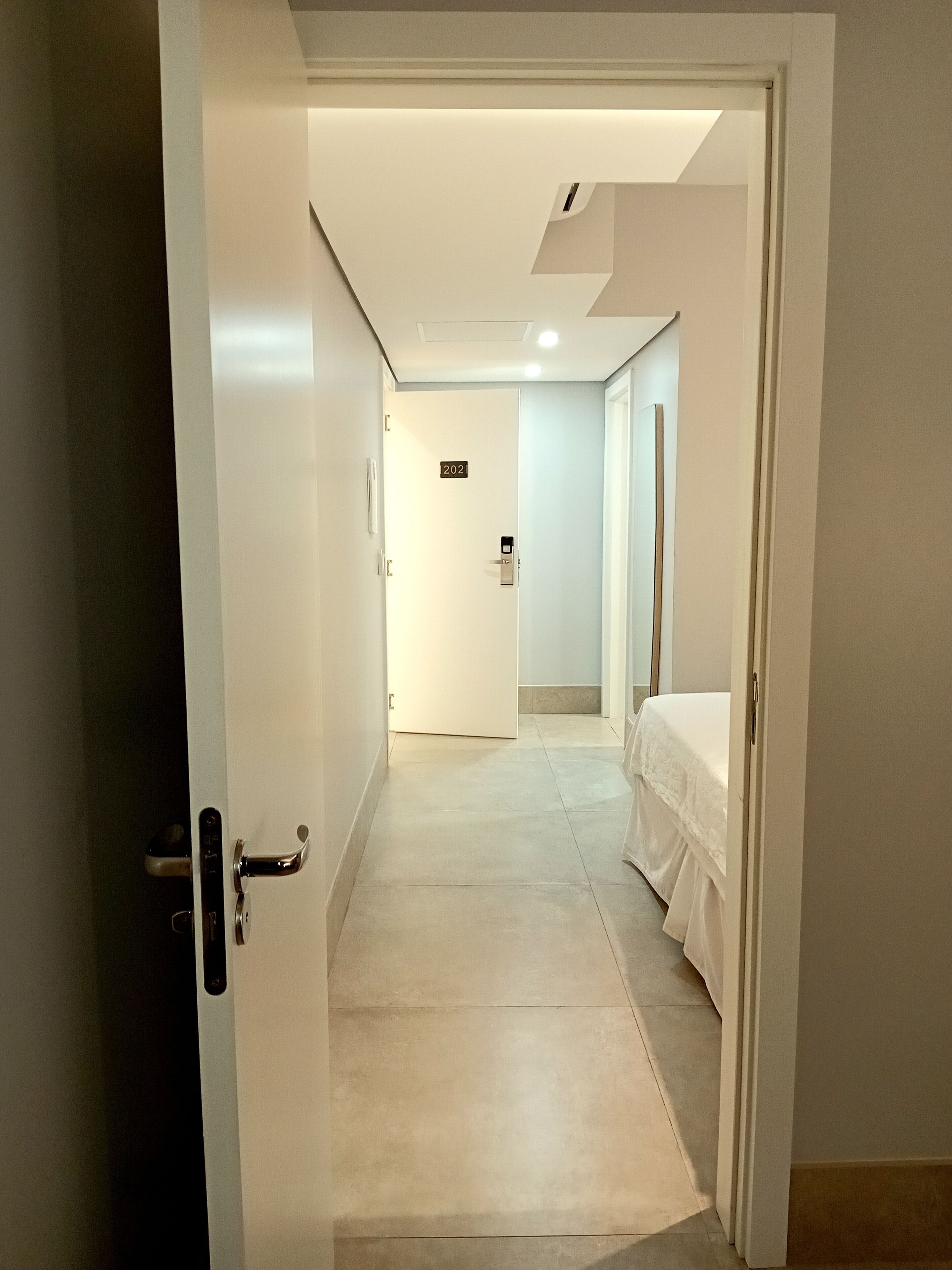 A hotel hallway with a door marked 202, a bed, and a light fixture on the ceiling.