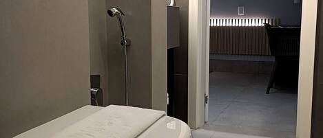 A modern bathroom with a freestanding bathtub, a towel on the seat, and a visible showerhead.