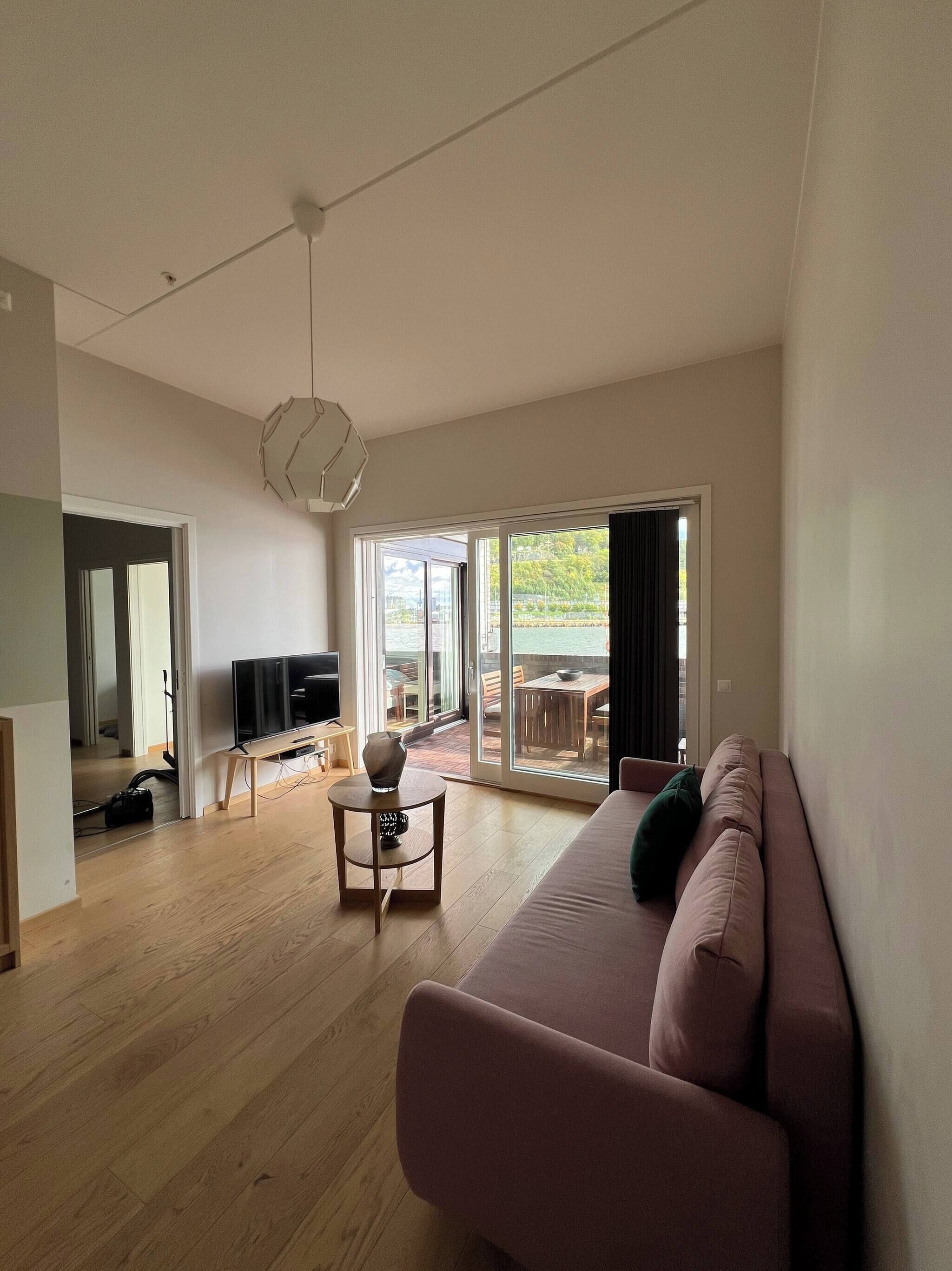 A modern living room with a sofa, a TV, a coffee table, and a view of the outdoors through a sliding glass door.