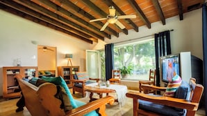 A cozy living room with wooden furniture, a ceiling fan, and a large window with curtains. - Family-Friendly Oasis with Pool (Cuernavaca)