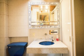 Un bany amb un vàter blau, un lavabo amb un mirall a sobre i un dosificador de sabó fixat a la paret.