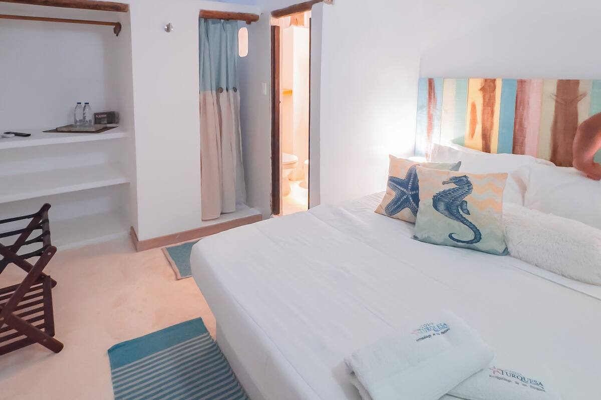 A bedroom with a bed, a wooden bench, a shelf with toiletries, and a view of the outside.