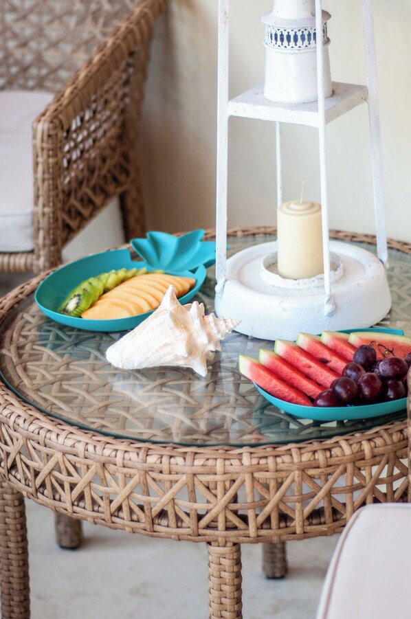 A wicker chair, a glass table with a candle, and a fruit bowl with watermelon and grapes. - Casa Turquesa (Los Roques)