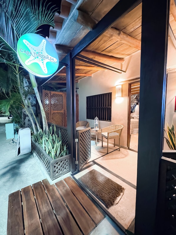 A wooden deck with a sign reading "CASA TURQUEÑA," a covered outdoor seating area with chairs and a table, and a staircase leading to an upper level. - Casa Turquesa (Los Roques)