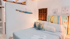 A bedroom with a bed, pillows, a wooden headboard, a small shelf, and a wall with nautical decorations. - Casa Turquesa (Los Roques)
