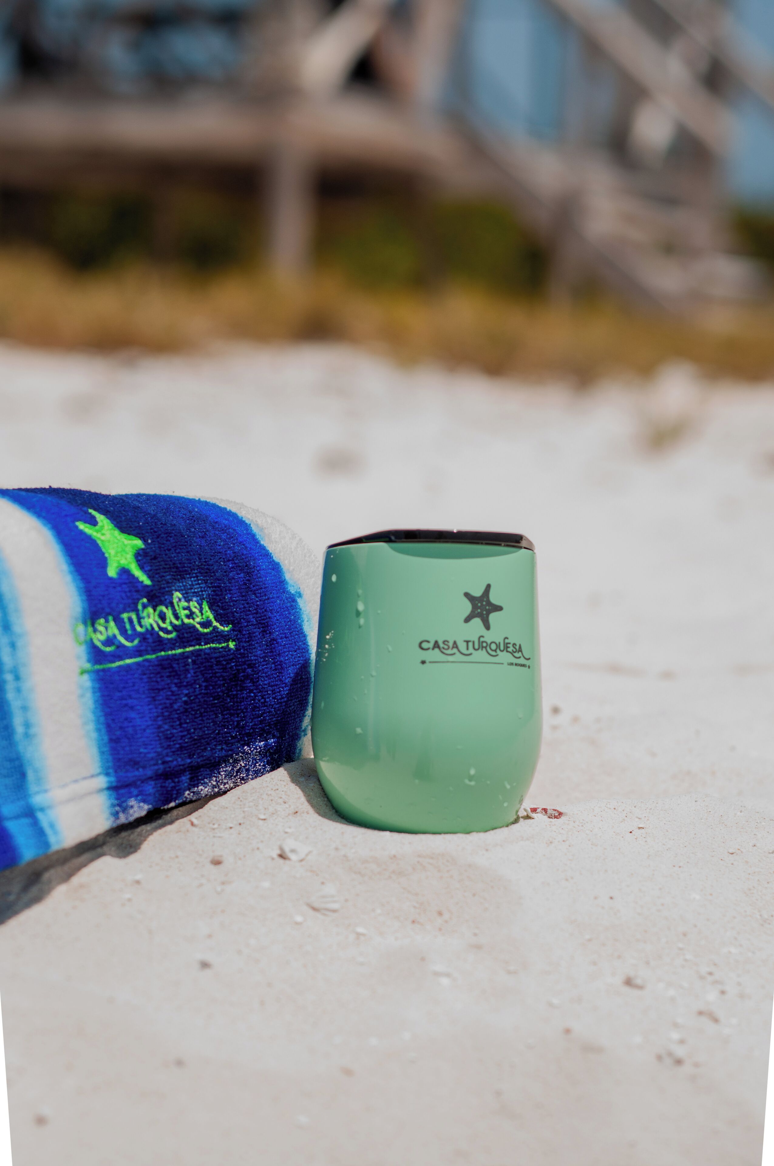 A green tumbler with the text "CASA TURQUESA" on a sandy surface.