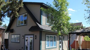 A two-story house with a front porch, a covered patio, and a wooden fence in the background. - Amazing Peace Chalet Oasis - Rockies Doorway / Easy 20 min commute Calgary South (High River)