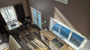 A modern kitchen with a large window, wooden flooring, and a dining area with a glass table and chairs. - Amazing Peace Chalet Oasis - Rockies Doorway / Easy 20 min commute Calgary South (High River)