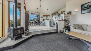 A modern living room with a fireplace, a dining area, and a kitchen. - Sunset Heights - Nelson Holiday Home (Nelson)