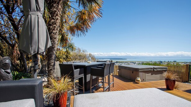 A rooftop terrace with a table and chairs, a hot tub, and a view of the ocean. - Sunset Heights - Nelson Holiday Home (Nelson)