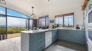 A modern kitchen with large windows, a wooden deck, and a view of the city. - Sunset Heights - Nelson Holiday Home (Nelson)