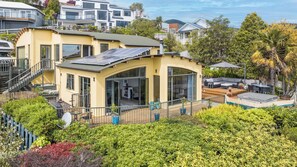 A modern yellow house with a deck, solar panels, and a view of neighboring houses. - Sunset Heights - Nelson Holiday Home (Nelson)