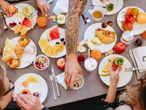 Un grupo de personas comiendo en una mesa con frutas, pasteles y bebidas diversas.