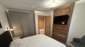 A bedroom with a bed, a grey wardrobe, a wooden door, a TV mounted on a wooden panel, and a grey chair. - Fantastic Apartment in the Kitzbuhel Alps (Mittersill)