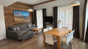 A modern living room with a wooden ceiling, a grey sofa, a wooden dining table with white chairs, and a TV on a shelf. - Fantastic Apartment in the Kitzbuhel Alps (Mittersill)