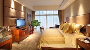 A hotel room with a bed, a television, a desk, a chair, a plant, and a window with curtains. - Hainan Guest House No.1 Building (Haikou)