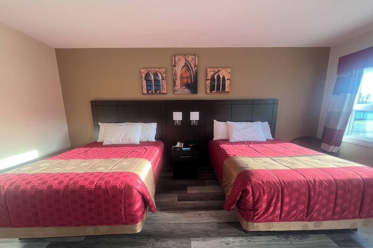 A hotel room with two beds, a wooden floor, a nightstand with a phone, and a window with curtains.