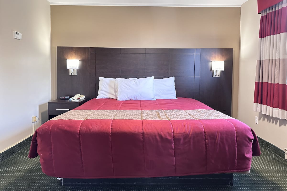 A hotel room with a large bed, a dark headboard, two bedside lamps, a telephone, and a window with curtains.