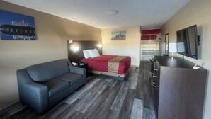 A compact hotel room with a bed, a sofa, a desk, and a TV.