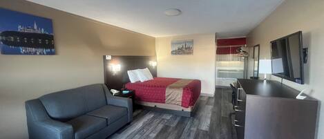 A compact hotel room with a bed, a sofa, a desk, and a TV.