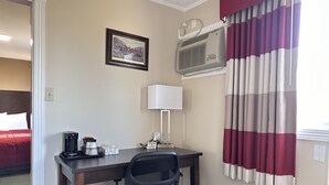 Ein Hotelzimmer mit Schreibtisch, Stuhl, Klimaanlage, Lampe und einem gerahmten Bild an der Wand.
