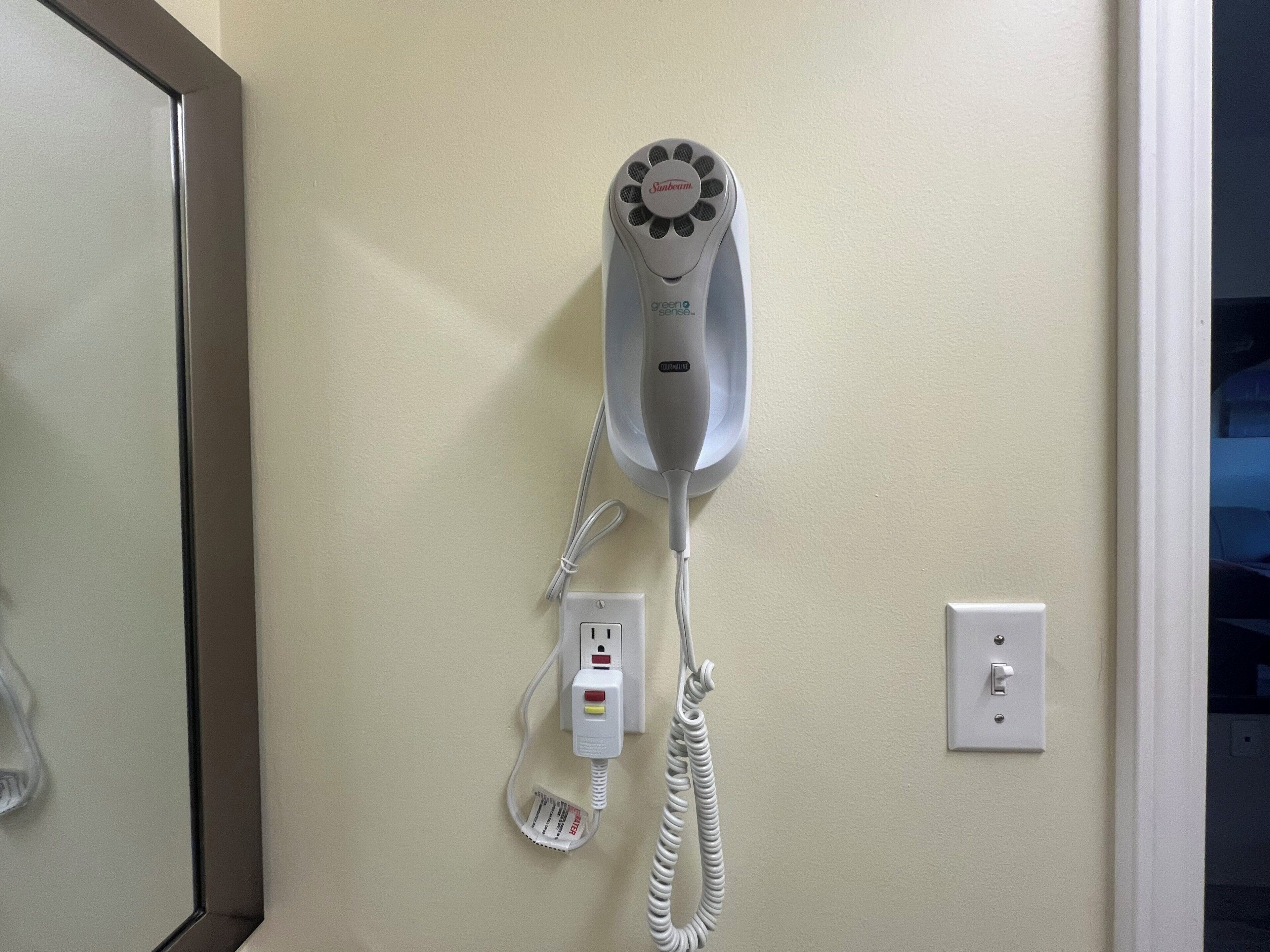 A hair dryer mounted on a wall with a power cord and a plug.