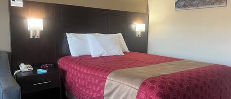 A hotel room with a large bed, two bedside tables, a nightstand, a clock, and a painting on the wall.