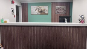 Ein Empfangsschalter mit einem Schild für 'Colonial House Motor Inn', einem gerahmten Gemälde von Pferden und einer kleinen Statue.