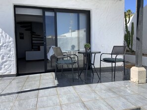 Eine Terrasse mit Tisch und zwei Stühlen, eine Glastür, die zu einem Innenraum führt, und eine Sukkulente in der Ecke.