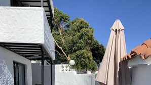 Un espace patio comprenant une table et des chaises, un mur blanc et une pergola surmontée d’un parasol blanc.