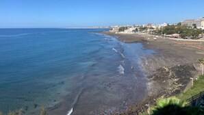 Une vue sur la côte, avec une plage, un ciel dégagé et des bâtiments en arrière-plan.