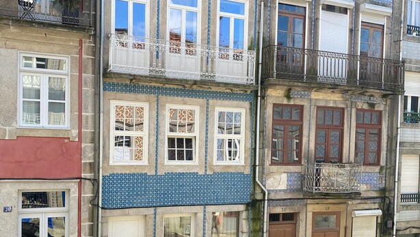 Une rangée de bâtiments européens traditionnels aux façades recouvertes de carreaux bleus et blancs, dotés de nombreux balcons, et bordée d’une rue pavée.