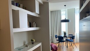 Une cuisine moderne avec des meubles blancs, un coin repas avec des chaises bleues et une grande fenêtre agrémentée de rideaux.