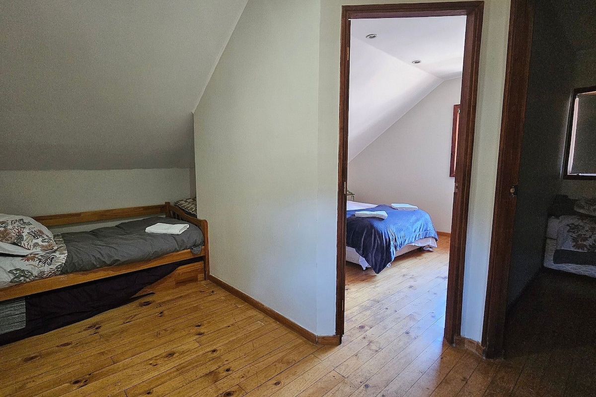 Ein kleines, einzelnes Zimmer mit schrägem Dach, Holzboden und einem Bett mit blauer Decke.