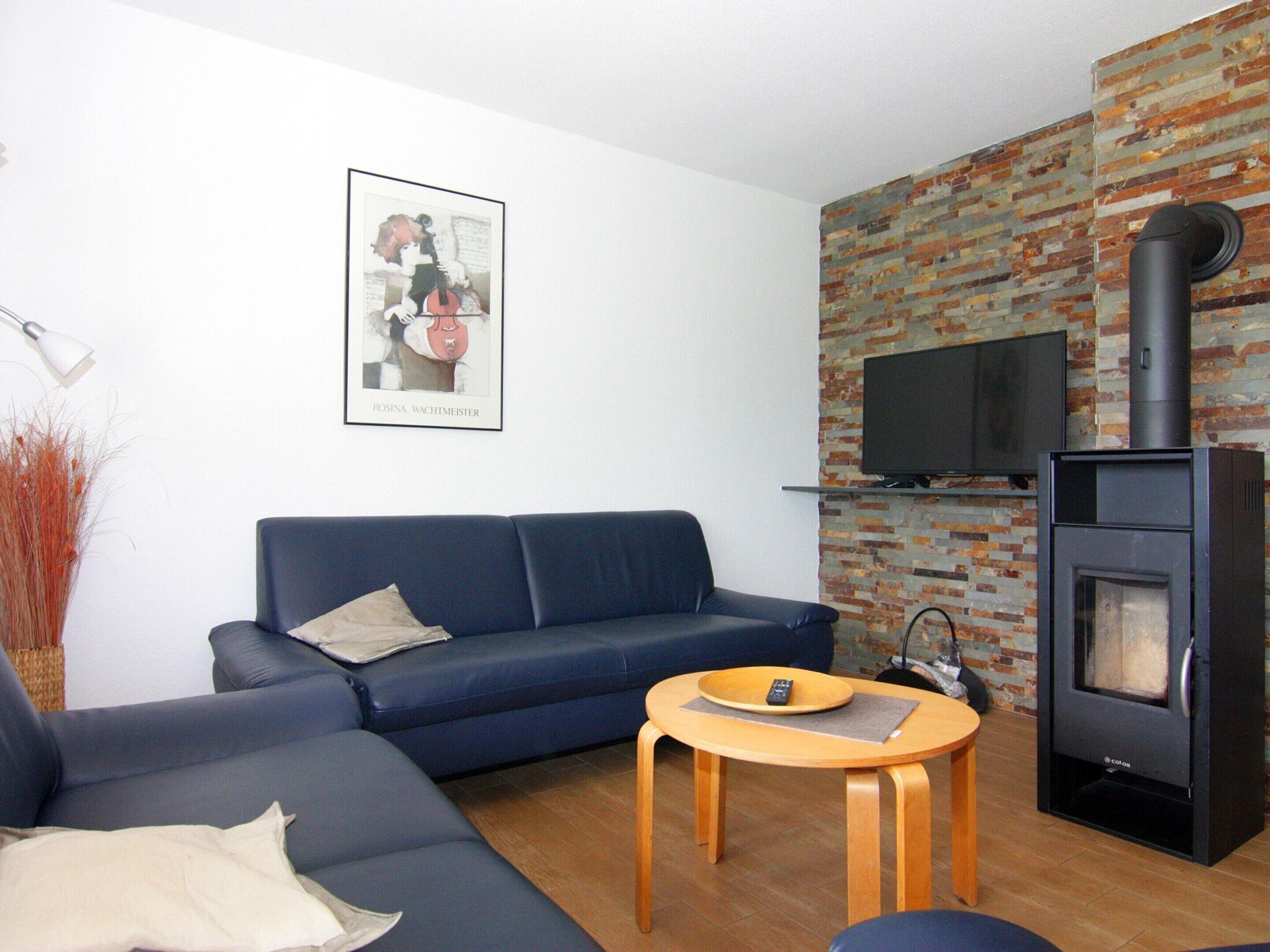 A living room with a blue sofa, a small wooden table, a fireplace, and a TV mounted on a brick wall.