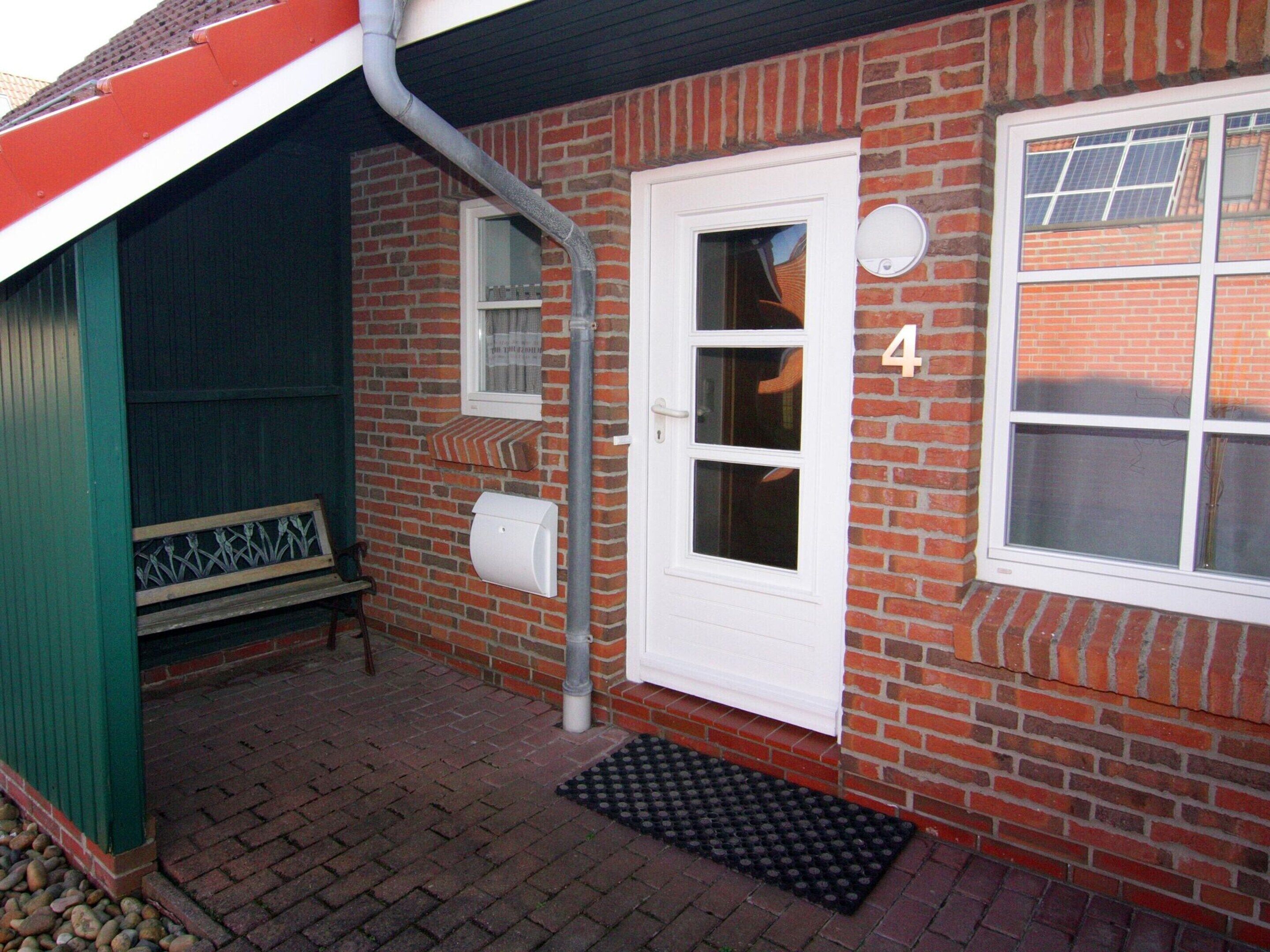 A brick house with a white door, a bench outside, and a number '4' on the wall.
