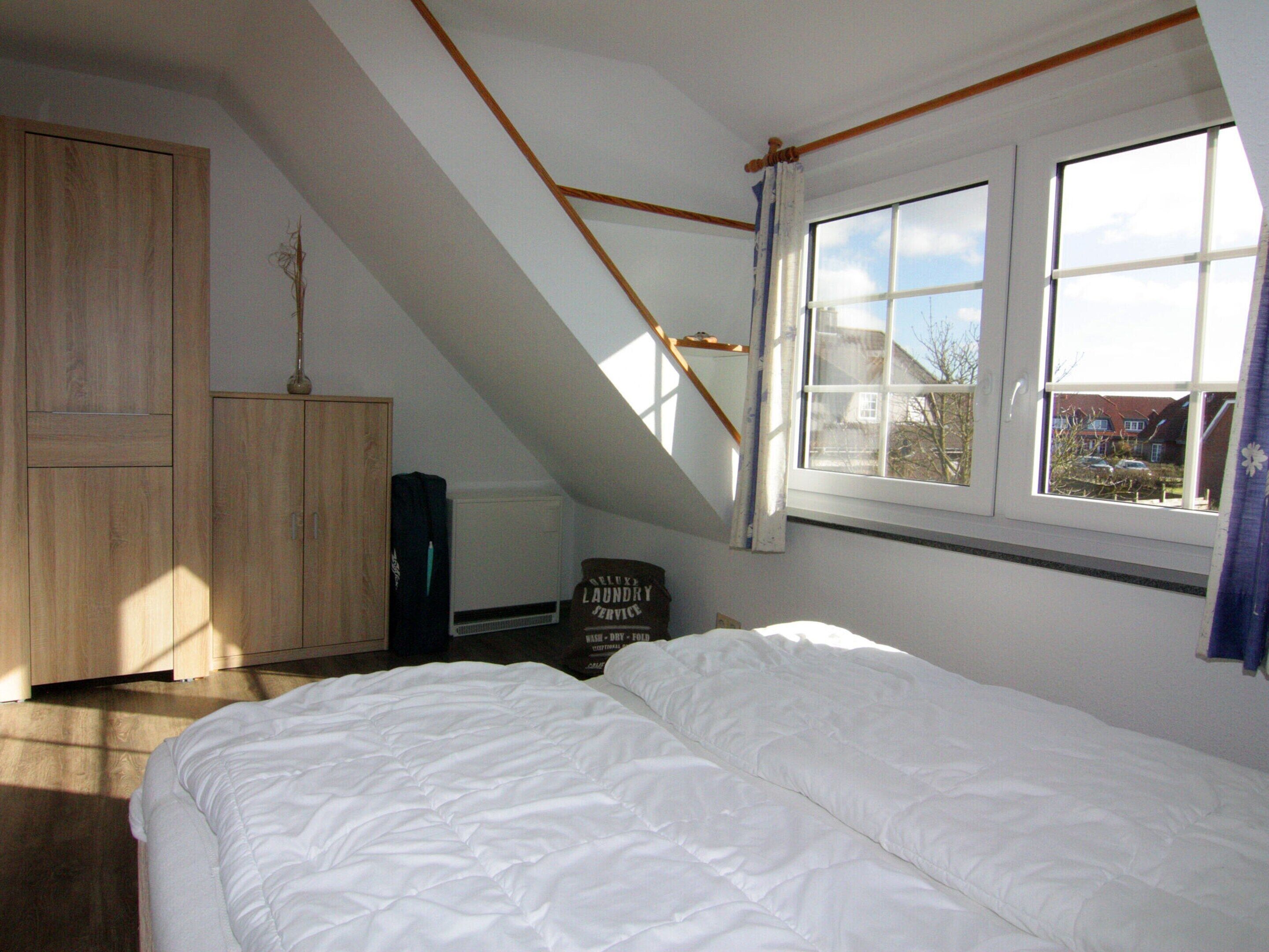 Une chambre avec un plafond en pente, un lit, une armoire et une fenêtre donnant sur l’extérieur.