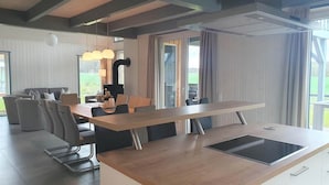 A modern kitchen with a central island, a dining area with a sofa and chairs, and large windows offering a view of the outdoors. - Ferienhaus im Skandinavischen Stil (Mirow)