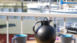 A balcony with a metal kettle and two mugs on a table, overlooking a marina with boats and a building in the background. - Holiday Complex Orther Reede - Fehmarn (Fehmarn)