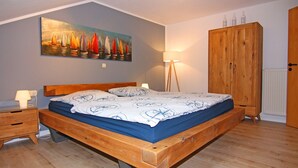 A bedroom with a wooden bed, a nightstand, a lamp, a wardrobe, and a painting on the wall. - Holiday Complex Orther Reede - Fehmarn (Fehmarn)