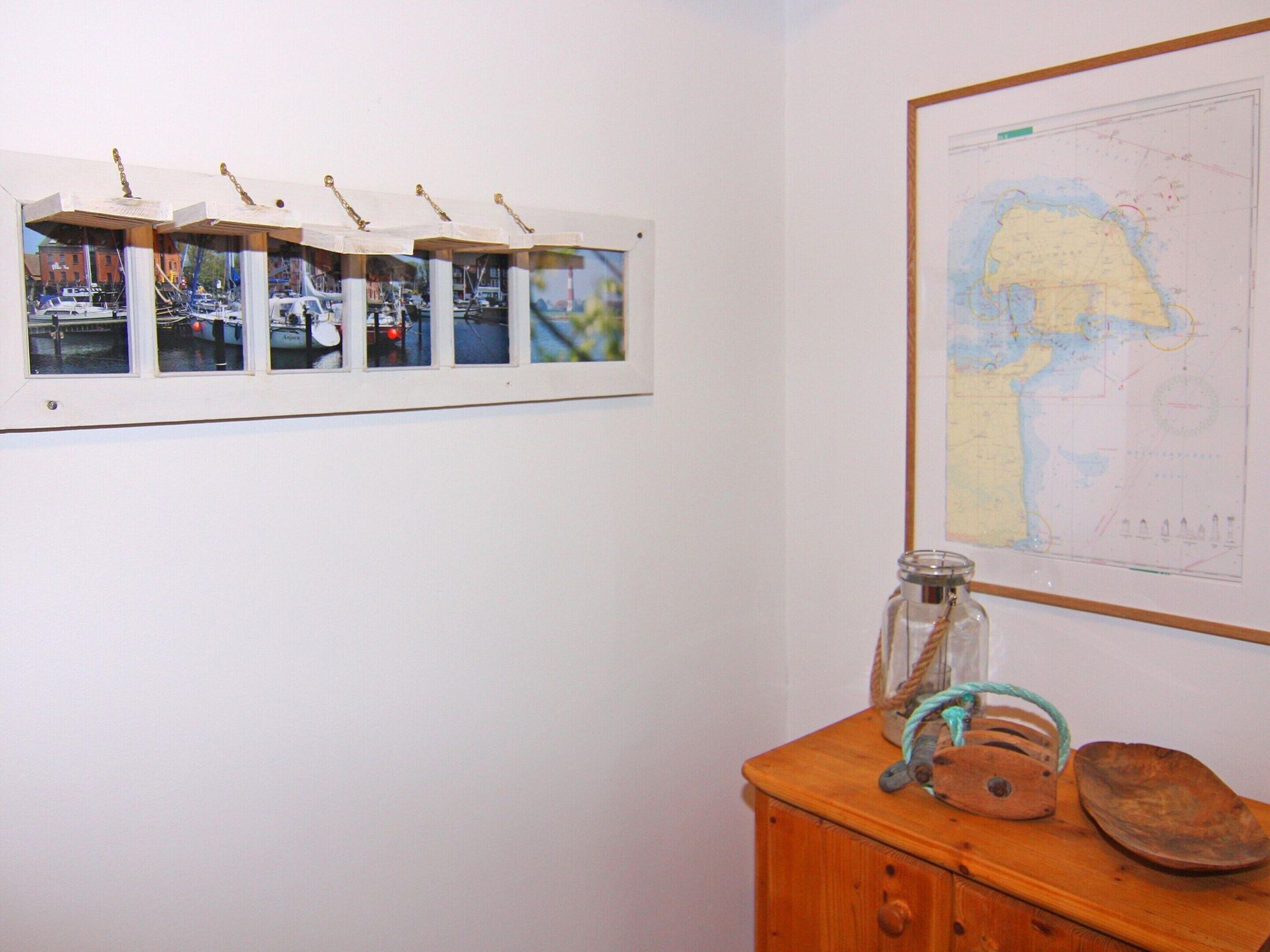 Una pared con varias fotografías enmarcadas, un mapa y un mueble de madera con un tarro y una cesta.