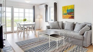 Een moderne woonkamer met een grijze bank, een salontafel en een eethoek met een witte tafel en stoelen.