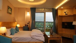 A hotel room with a bed, bedside lamps, a desk, a television, and a view of the outside.